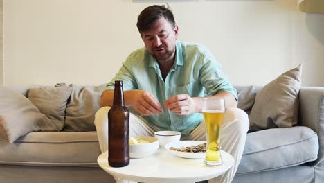 man relaxing on couch with beer and snacks