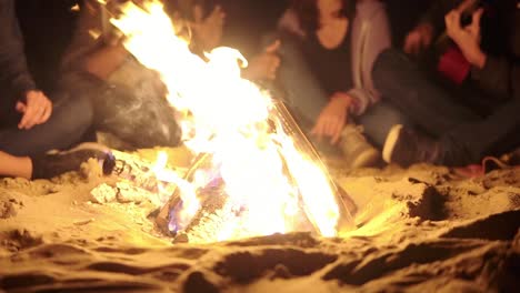 Close-Up-view-of-the-bonfire-late-at-night.-Young-people-sitting-by-the-fire-in-the-evening.-Cheerful-friends-singing-songs-and