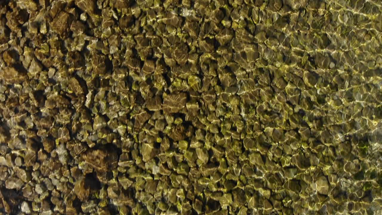 Texture of lake bottom with pebbles reflecting sunrays on transparent vibrant water