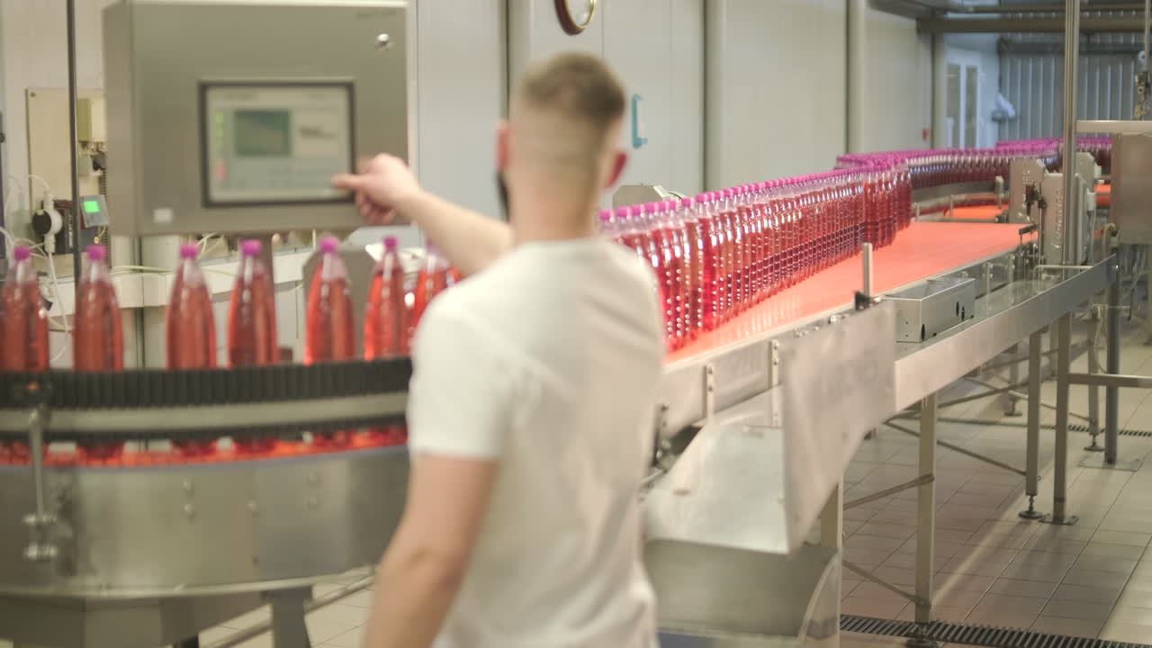 Man Operating Control Panel in Beverage Factory with Bottles on Conveyor