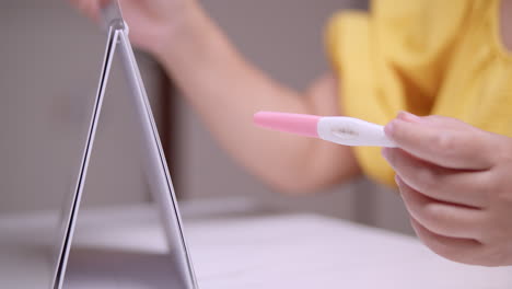 Expectant-mother-going-through-a-calendar-to-count-the-weeks-to-her-expected-due-date-while-holding-a-pink-pregnancy-test-kit-on-her-left-hand