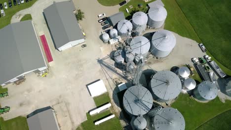 aerial view looking down over industrial indiana agribusiness ranch orbiting steel silo storage tanks