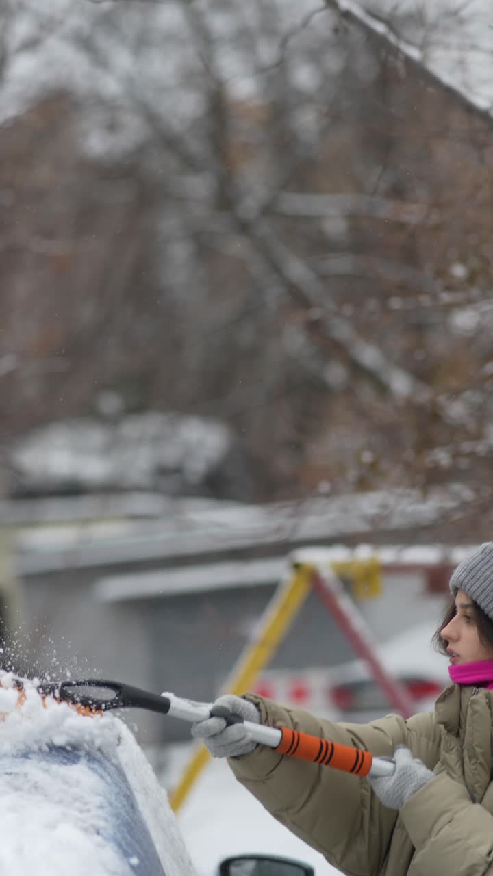 mujer quitando la nieve del parabrisas de un coche en invierno