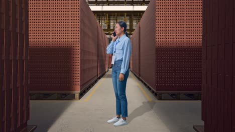 full body side view of asian female with red brick packed in stacks are stored, she is speaking with someone in the phone