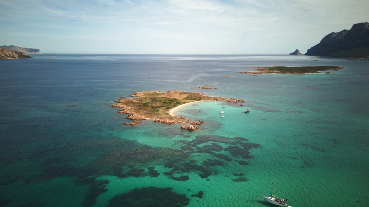 Stunning drone timelapse of a rocky island in clear turquoise waters off Sardinia, Italy, with Tavolara in the background and boats anchored nearby