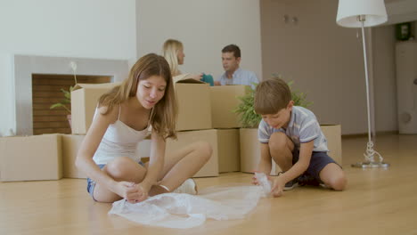 niños lindos sentados en el suelo y estallando envoltura de burbujas después de moverse