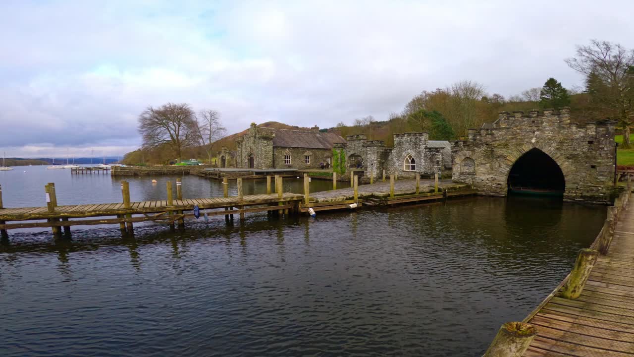 Lake Windermere in the English Lake District, with its iconic wooden jetty, historic stone-built buildings, and moody grey skies