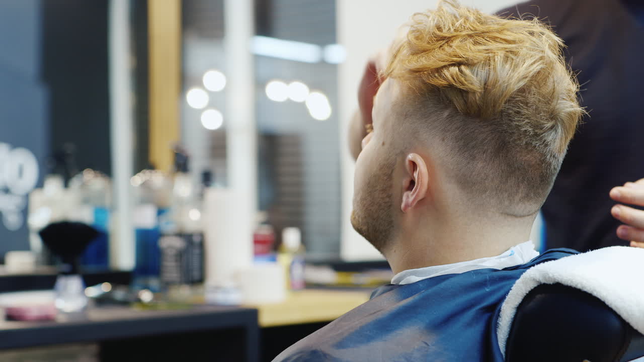 En ung mand får lavet hårstyling i salonen – set bagfra.
