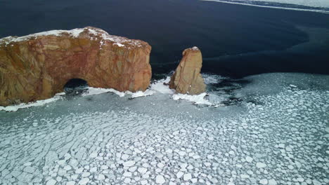 Luftaufnahme-Des-Percé-Felsens-Im-Winter-Mit-Eis-Auf-Dem-Ozean