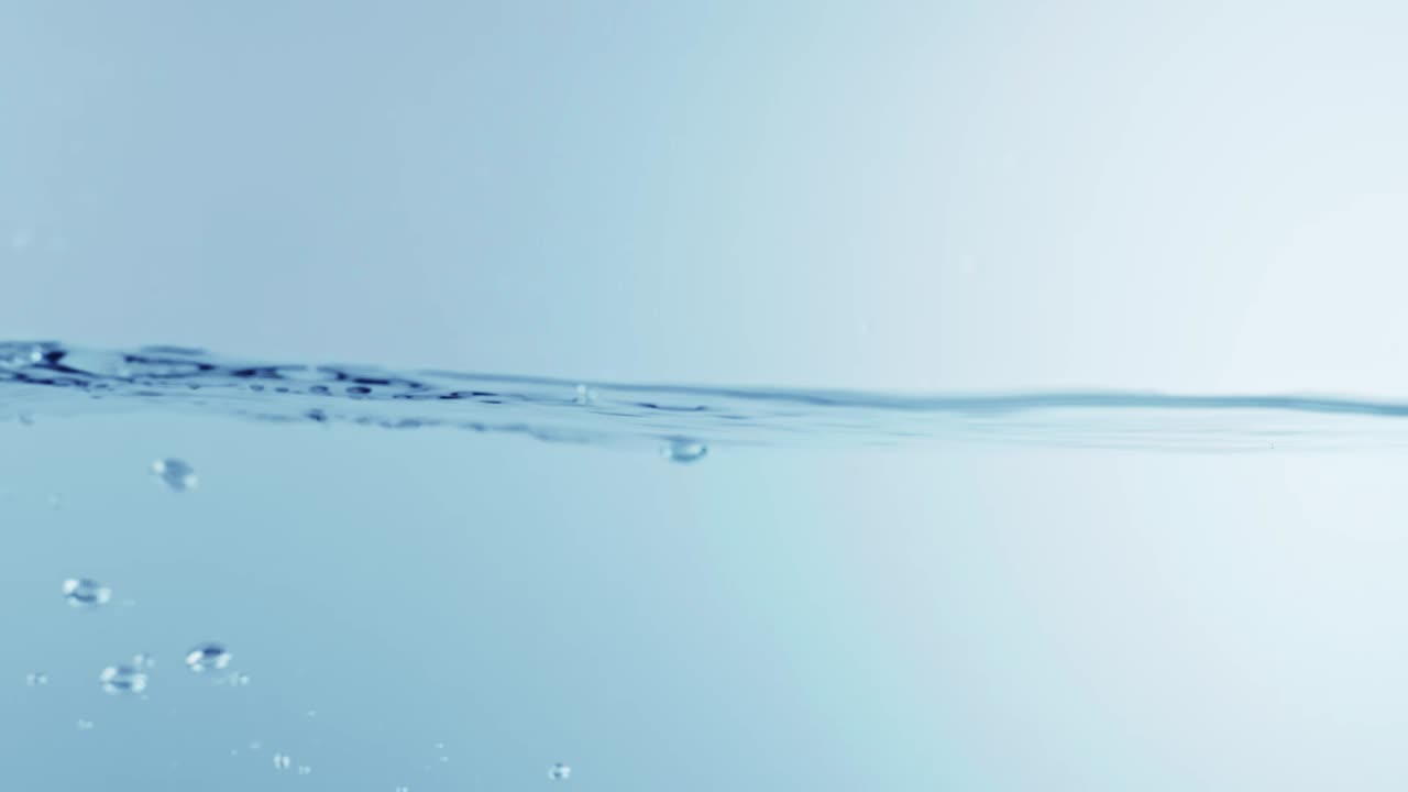 슬로우 모션의 깨끗한 물 표면은 물이 튀는 상점으로 화면을 채우고 기포로 액체 표면을 흔들고 있습니다.