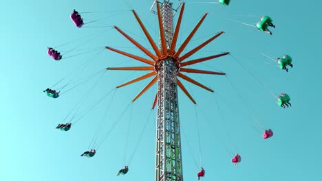 people riding vertical chain swing ride in amusement park, tilt up, day