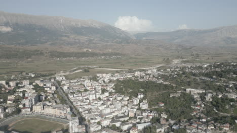 drone shot above the city gjirokaster albania on a sunny day with haze in the air and the city of white houses underneath and mountains and clouds in the background log