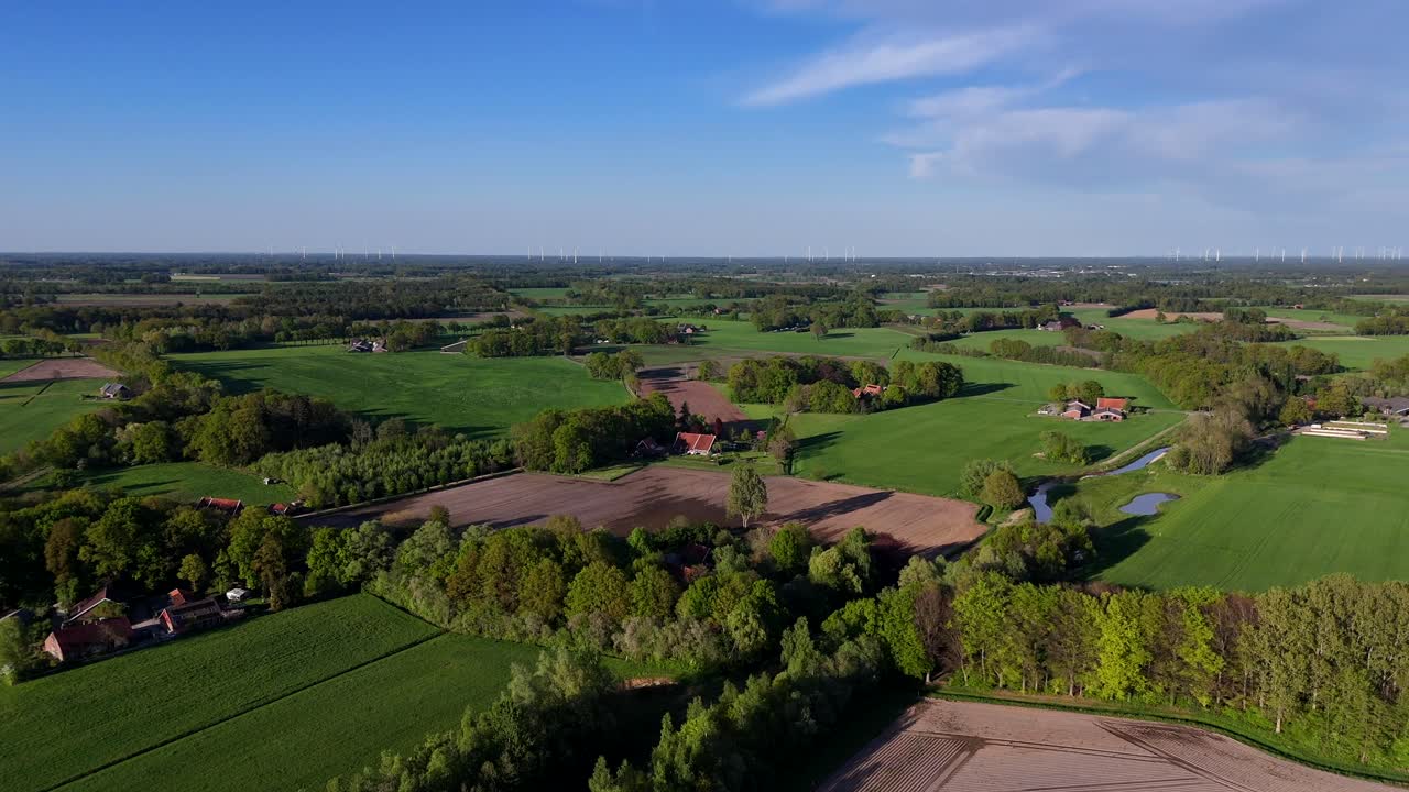 Different colored agricultural farm fields in american with flowing river. Sunset time with blue sky in springtime. Forest trees, suburb neighborhood with farmers house. Aerial wide shot.Drone footage