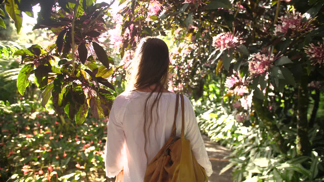 siguiendo a una hermosa mujer caminando entre árboles tropicales en flor.
