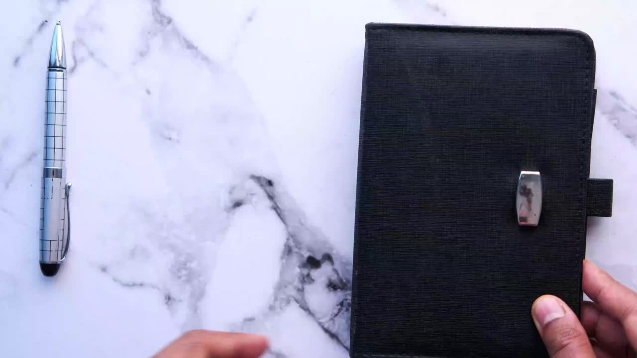 Open black notebook with pen on marble surface