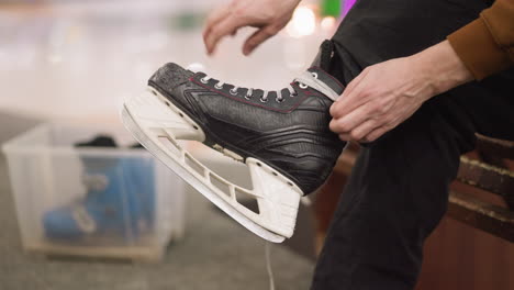 a close view of someone loosening the laces of a black ice skate, with a blue skating shoe visible in a transparent container in the background, having a blur light view