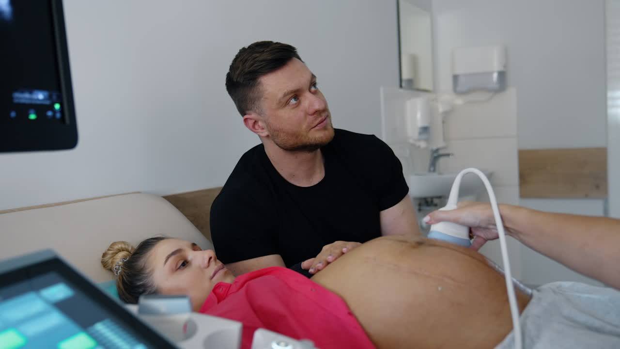 Future parents attentively look on the screen in doctor's cabinet. Caucasian couple is on the ultrasound pregnancy check up.