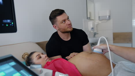 future parents attentively look on the screen in doctor's cabinet. caucasian couple is on the ultrasound pregnancy check up.