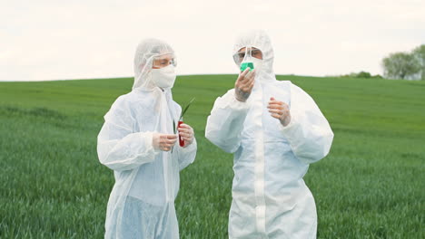 caucasian researchers in protective suit holding test tubes and tree branch while doing pest control in the green field