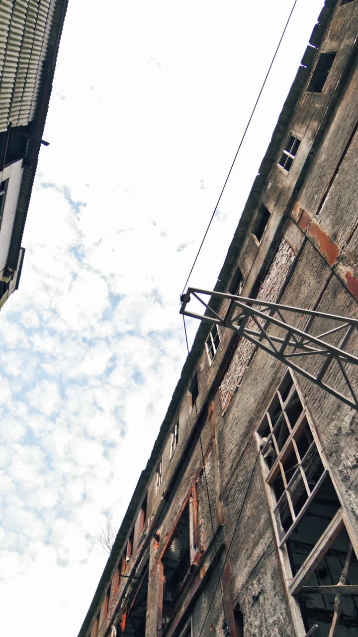 Old abandoned plant with broken windows ruined after the military actions. Demolished plant with pitted roof and some snow on the ground in winter. Bottom view Vertical video
