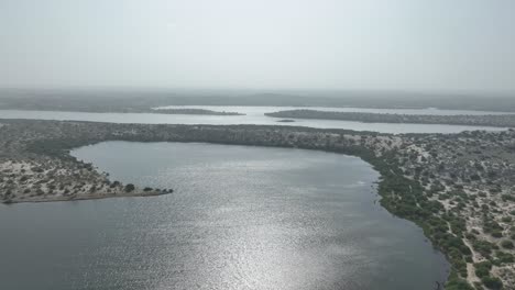 Filmación-Aérea-Reveladora-Cinematográfica-Del-Lago-Botar-Con-Reflejo-Del-Sol-En-El-Lago-Y-Plantas-Silvestres-En-Pakistán