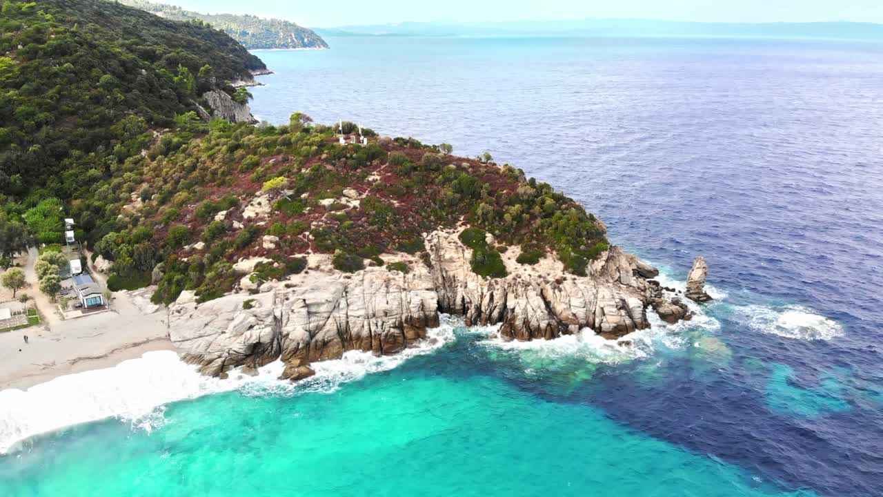 Aerial drone view of the Aegean sea coast with camping near the beach, multiple greenery, hills on the background, blue water with waves. Greece