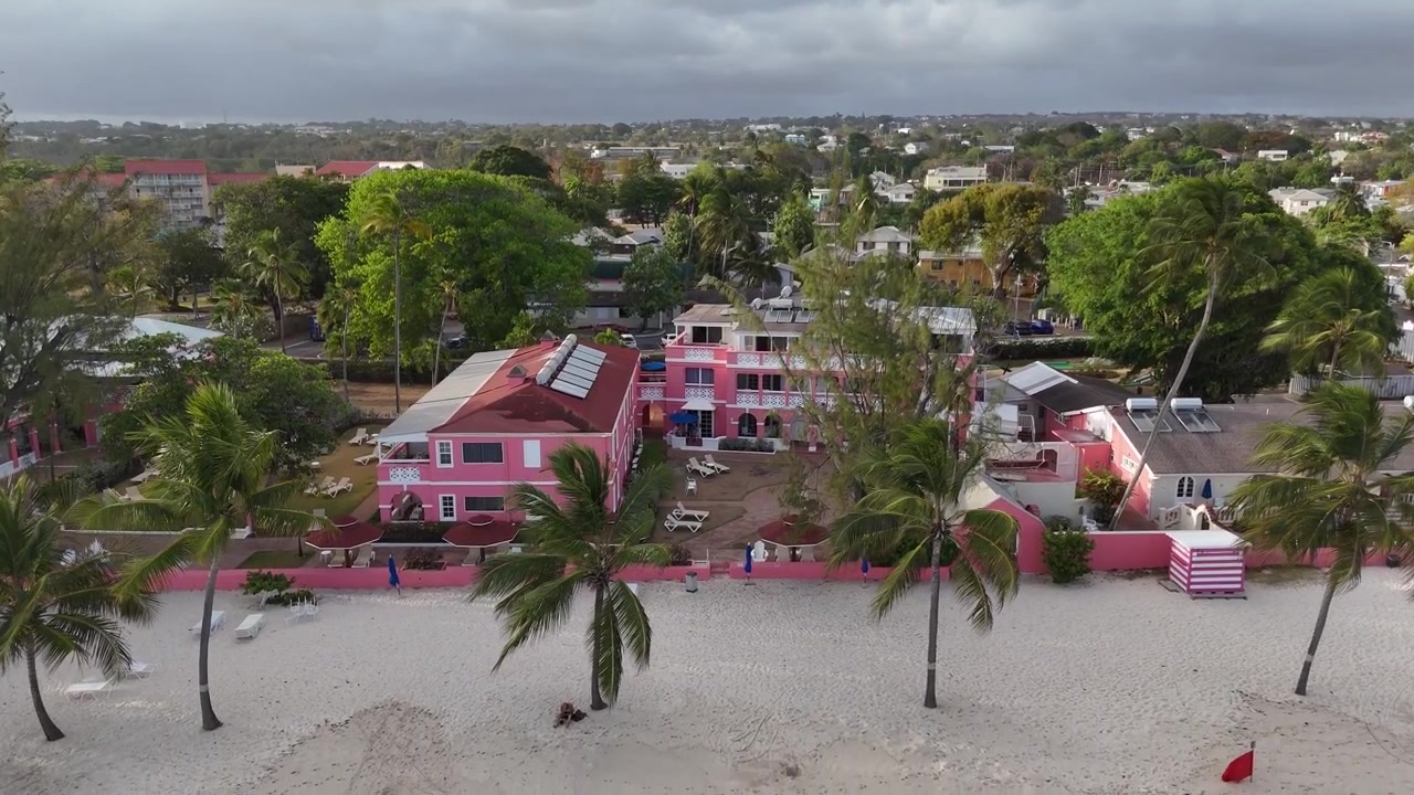 Vista aerea con drone da bassa angolazione che riprende hotel resort colorati fronte mare e lussureggianti palme verdi presso la spiaggia di St Lawrence Gap nella destinazione Bridgetown, Barbados.