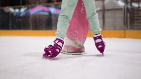 nahaufnahme von jemandem, der auf einer eislaufbahn schaitst und lila schlittschuhen und aschfarbene hosen trägt. die szene zeigt die dynamische bewegung und das gleichgewicht beim schlittschießen mit einem rosa objekt