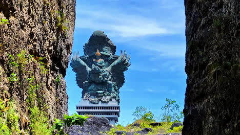 garuda wisnu kencana statue seen through rocky cliffs in bali, clear sky background