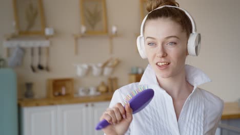 woman singing and dancing in kitchen with headphones and hairbrush