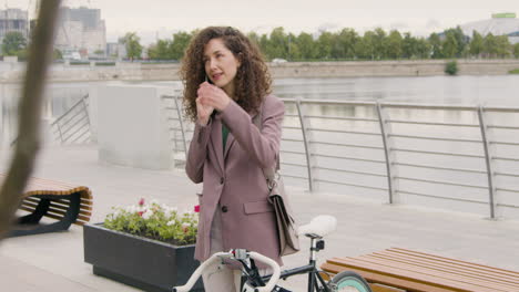 Mujer-Rizada-Con-Ropa-Formal-Y-Bicicleta-Hablando-Por-Teléfono-Móvil-En-El-Puente-De-La-Ciudad-1
