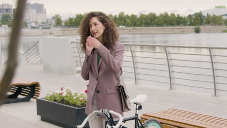 mujer rizada con ropa formal y bicicleta hablando por teléfono móvil en el puente de la ciudad 1