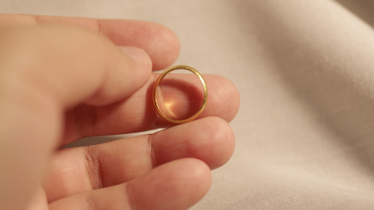A hand holding a simple golden ring