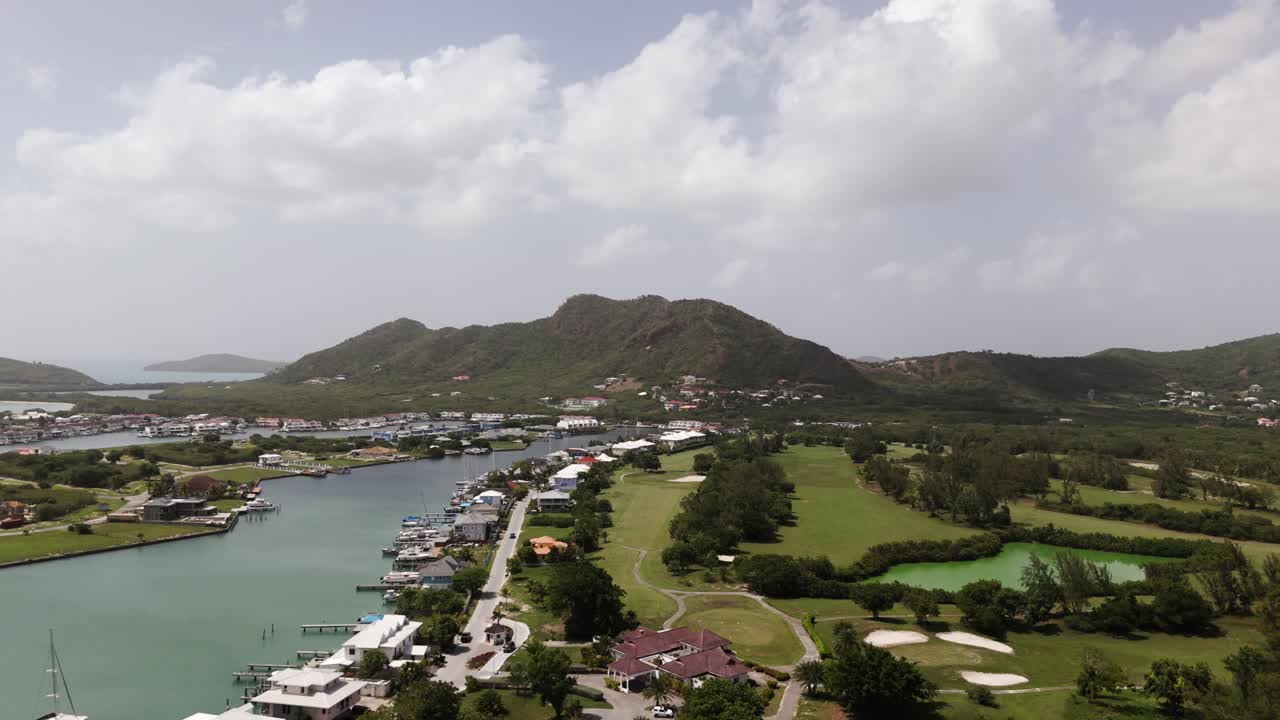 Jolly harbor, antigua with marina, golf course, and lush hills on a sunny day, aerial view