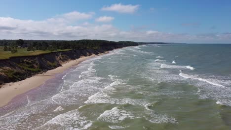 Flying-Over-Coastline-Baltic-Sea-Ulmale-Seashore-Bluffs-Near-Pavilosta-Latvia-and-Landslides-With-an-Overgrown,-Rippling-Cave-Dotted-Cliff-and-Pebbles