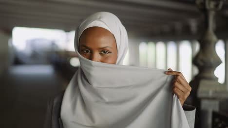 happy black woman hides face behind hijab under bridge