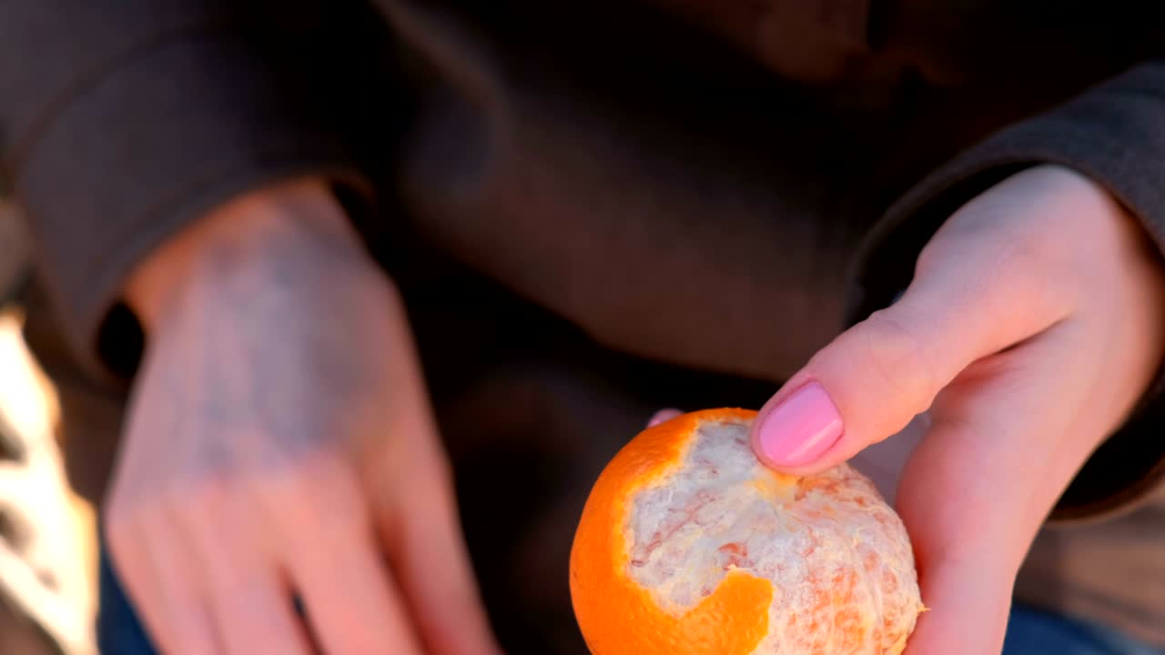 클로즈업 여성의 손이 공원에서 만다린을 질을 벗는다.