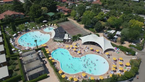 Toma-Aérea-De-Personas-Nadando-En-La-Piscina-Del-Camping-Europa-Silvella-En-El-Lago-De-Garda,-Italia