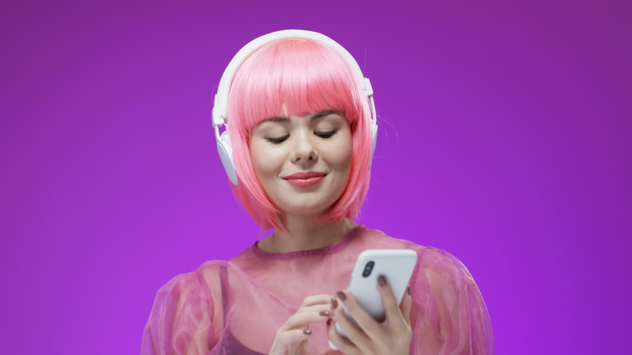 hermosa mujer con una peluca rosa y grandes auriculares con teléfono inteligente en las manos, bailando y riendo