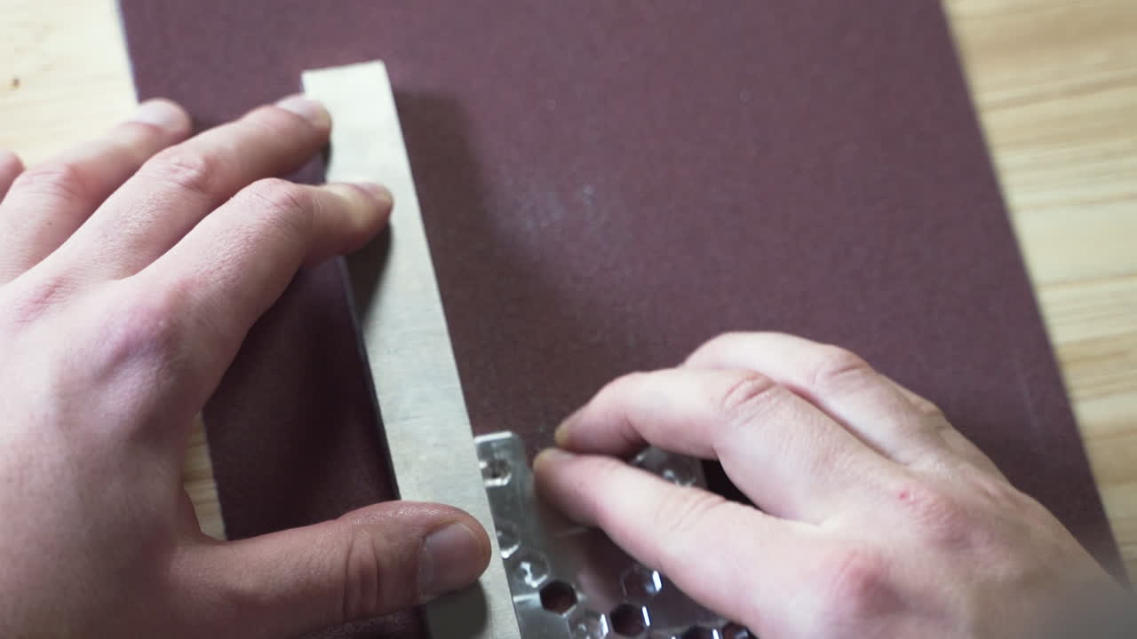 Hands smoothing a metal plate with a whetstone on sandpaper, close up