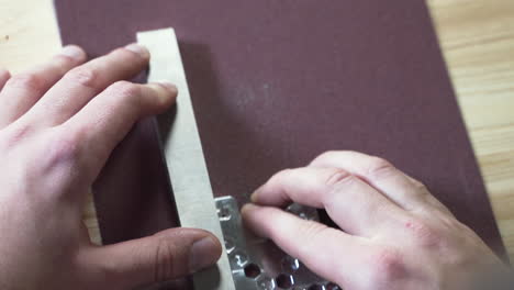 hands smoothing a metal plate with a whetstone on sandpaper, close up