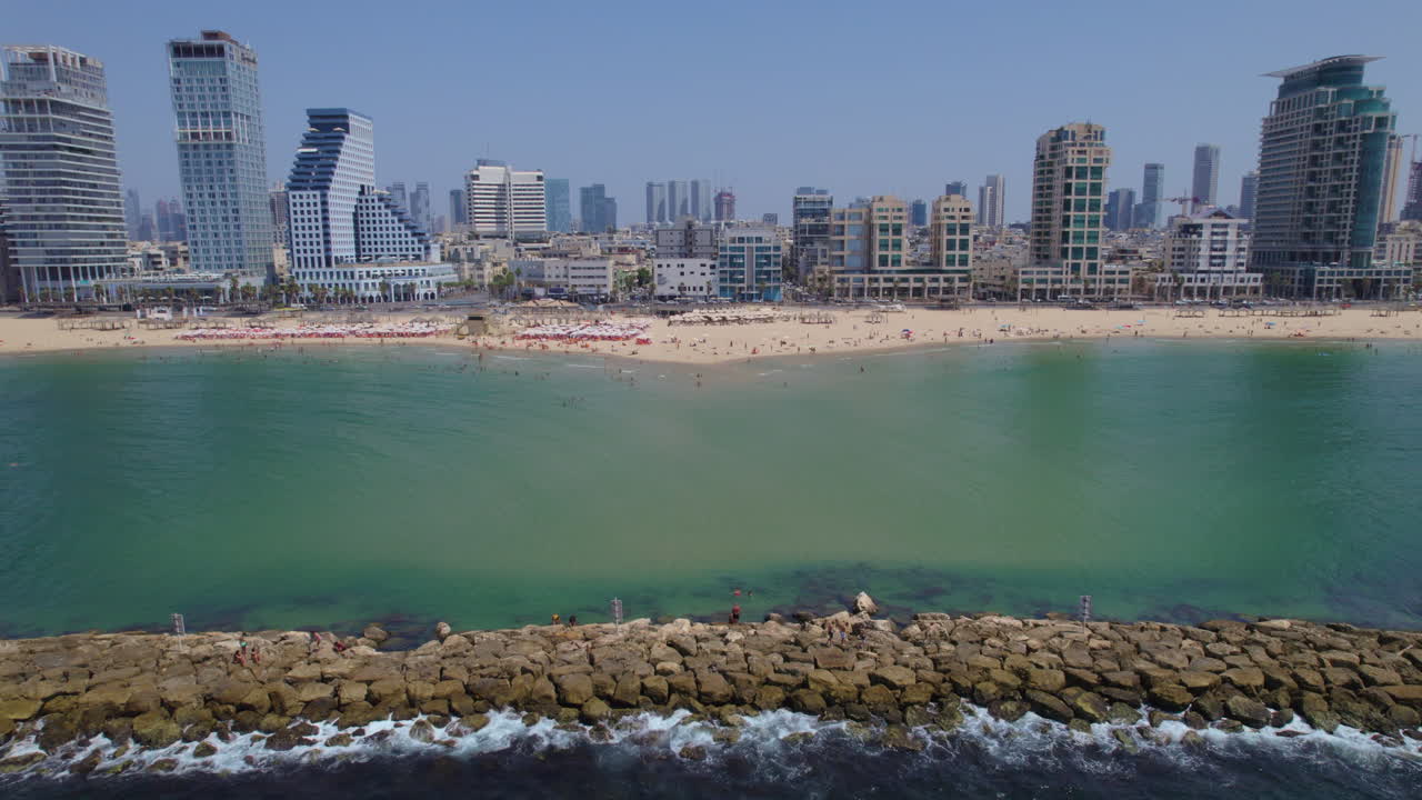 Calm and multicolored view of Tel Aviv's beaches from the sea side near the breakwaters, lots of people resting under white umbrellas