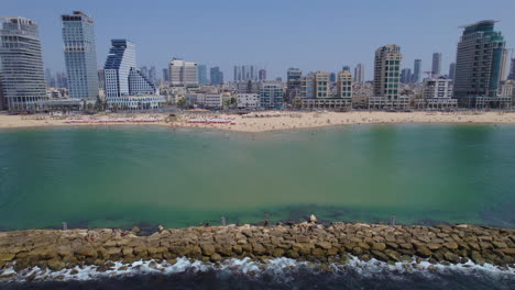 vista tranquila y multicolor de las playas de tel aviv desde el lado del mar cerca de los rompeolas, mucha gente descansando bajo paraguas blancas