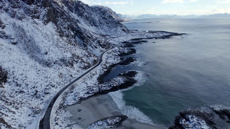 aerial dolly shot along the scenic route andøya with waves crashing on the beach and snow covered mountains