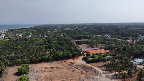 aerial footage of tranquil rural coastline in south india. the scene is dominated by a dense, verdant canopy of coconut and palm trees that stretches inland from a pristine sandy beach on the left
