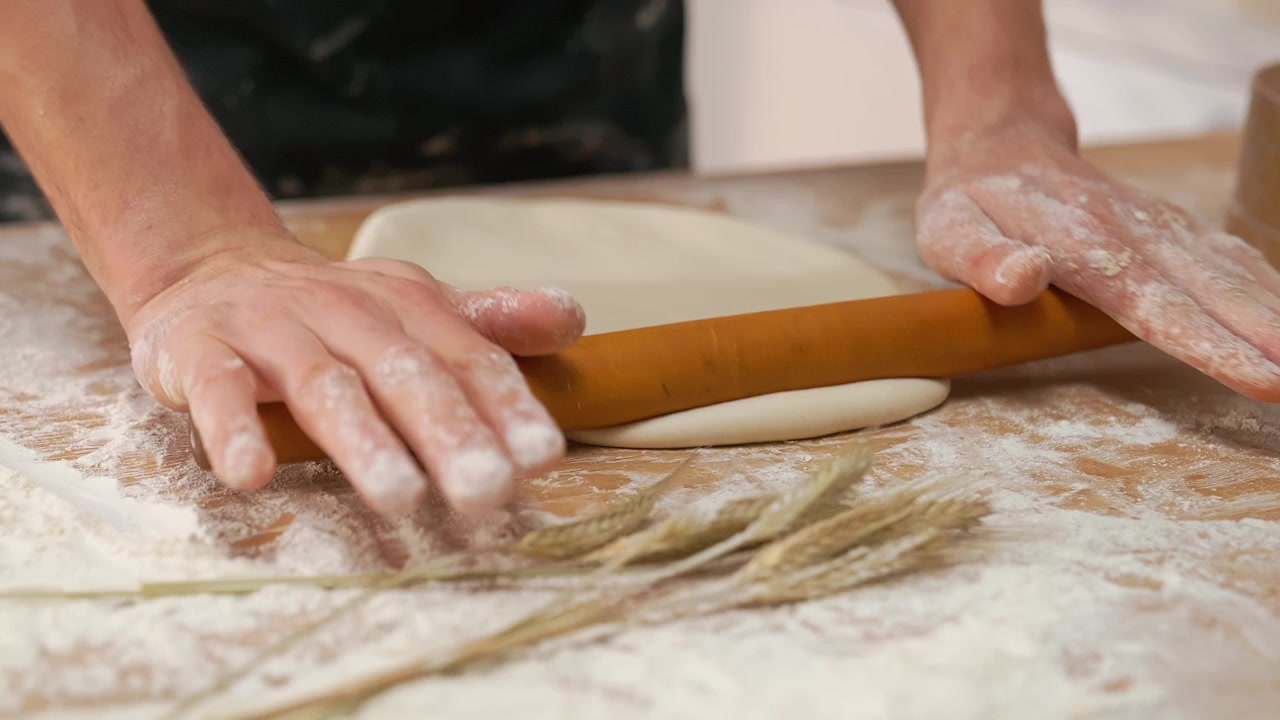 Mani che stendono impasto fresco su un tavolo di legno infarinato