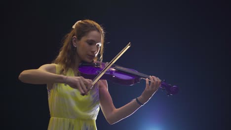 young woman masterfully plays the violin on a dark stage.