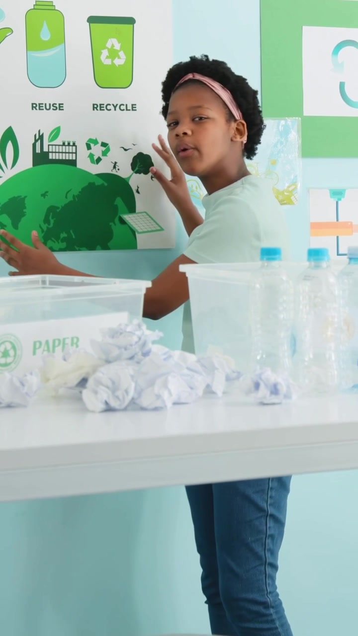 Vertical video: Camera starting kid in green shirt sorting paper pointing to reuse signs at school