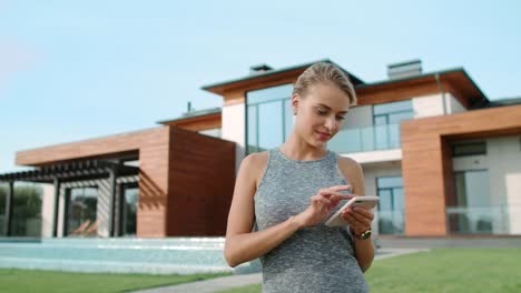 Mujer-Relajada-Enviando-Mensajes-De-Texto-Al-Móvil-Cerca-De-Una-Casa-De-Lujo.-Mujer-Bonita-De-Pie-Cerca-De-La-Villa