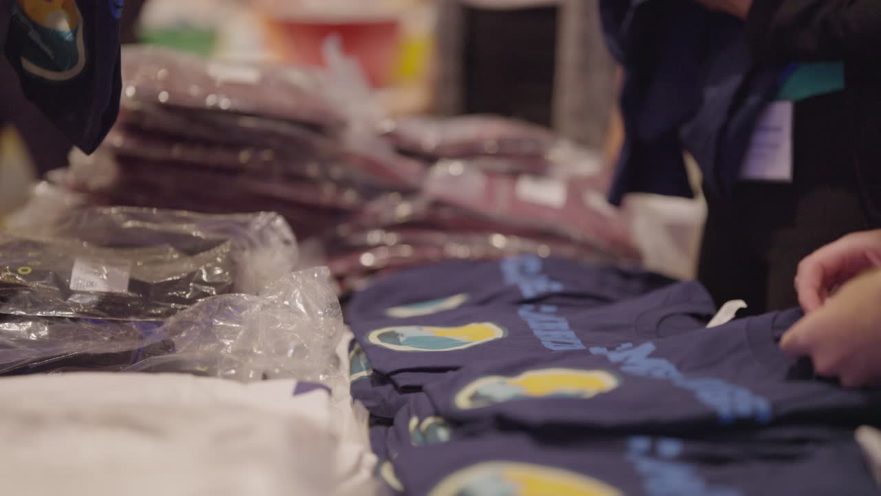 Una pila di nuove T-shirt, alcune imbustate, altre aperte, sono presentate su un tavolo a disposizione degli invitati all'evento.